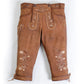 Brown suede lederhosen worn with suspenders, featuring decorative embroidery, front flap closure, and knee-length design