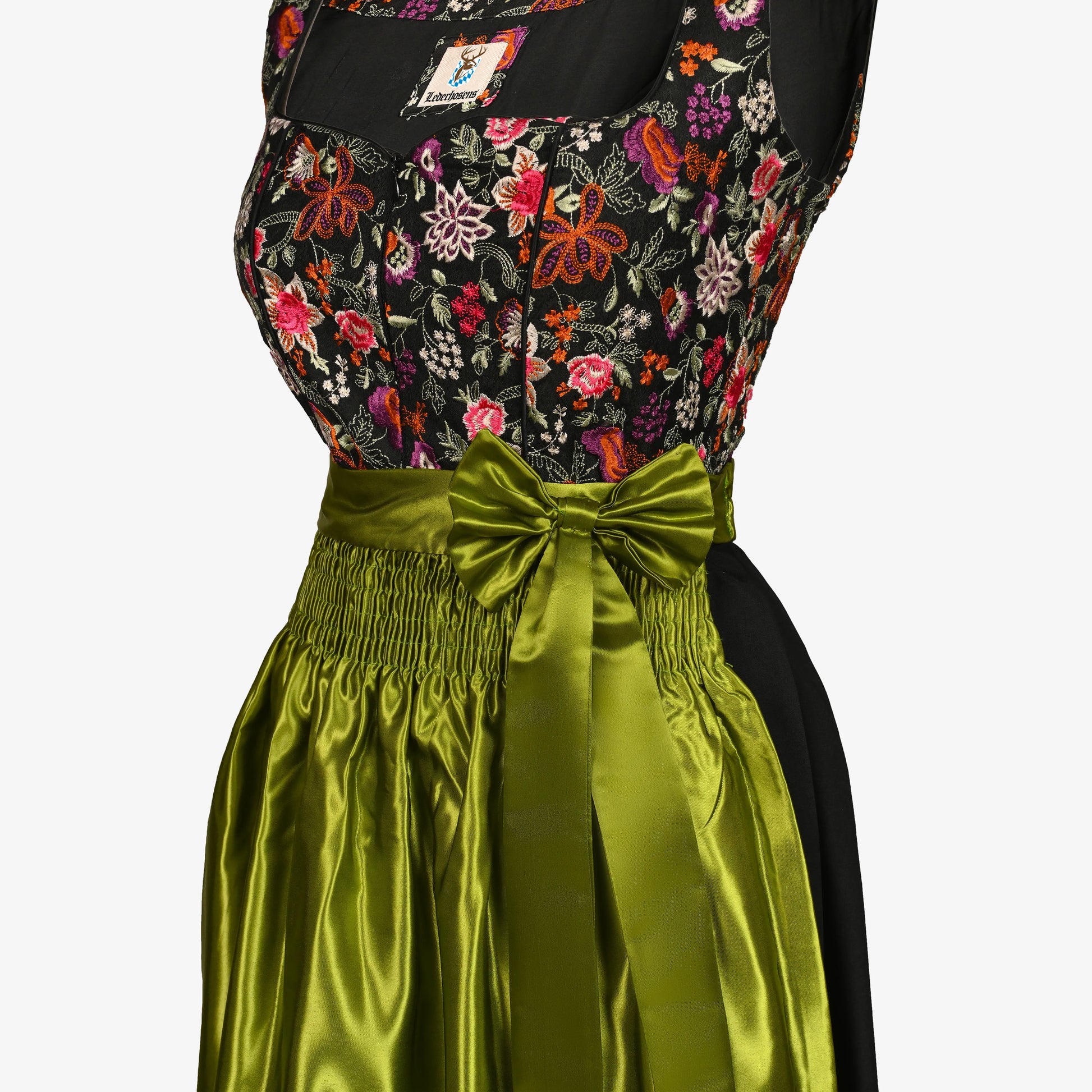 A close-up of a traditional German dirndl dress featuring a black bodice with a vibrant multicolor floral embroidery pattern and a wide, shiny olive green satin skirt with a large bow at the waist.